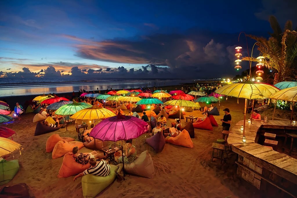 Seminyak, Indonesia - February 25, 2016: Seminyak beach at dusk. People chilling out, having drinks, laying on puffs, under colourful lit parasols