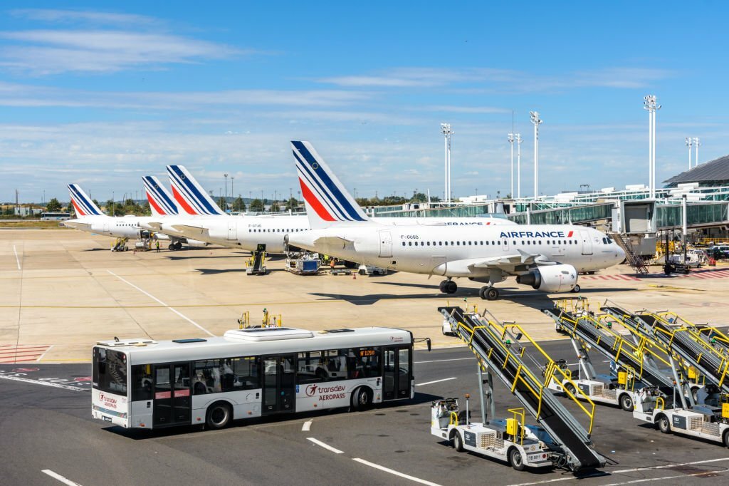Roissy-en-France, France - July 27, 2020: A shuttle bus is driving on Paris-Charles de Gaulle Airport between belt loaders and Air France airliners stationing on the apron area by the Terminal 2F.